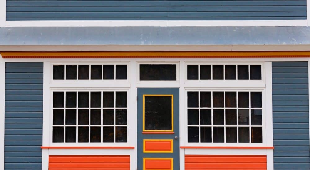 Symmetrical view of the front door and entrance to a quaint colorful wooden house with large cottage pane windows on either side