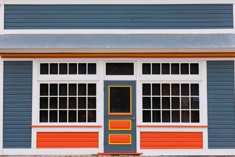 Symmetrical view of the front door and entrance to a quaint colorful wooden house with large cottage pane windows on either side